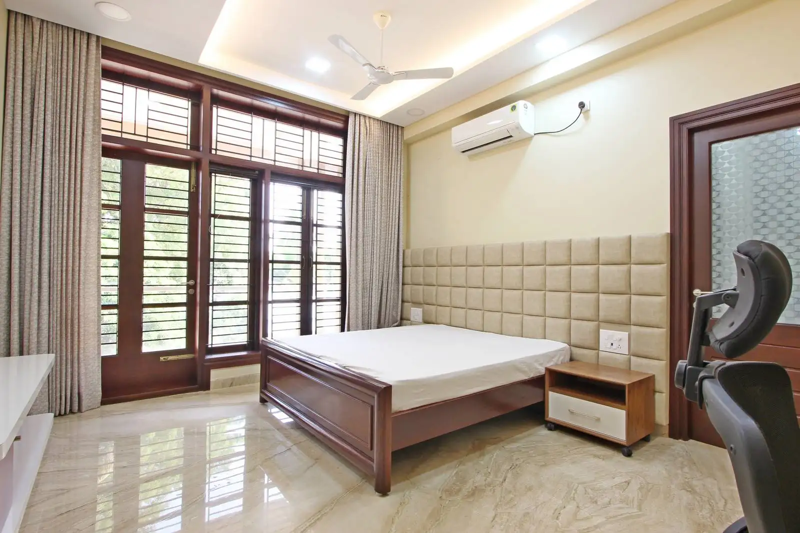 Spacious and bright bedroom with a feature wall, floor-to-ceiling windows, and a versatile layout that combines comfort, natural light, and a functional workspace.