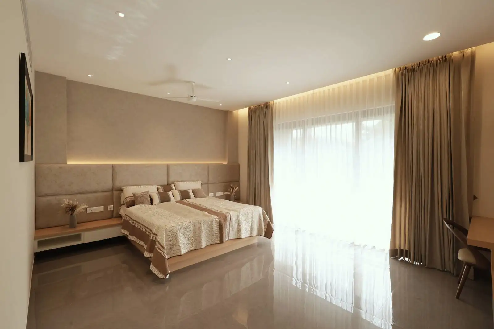 The bedroom features a large window that invites natural light and outdoor views, while an upholstered headboard wall with subtle backlighting adds elegance and visual depth.