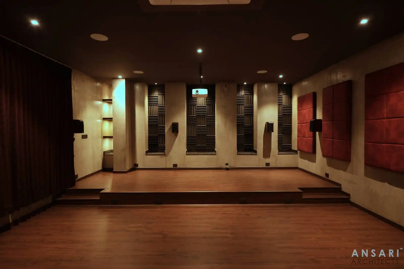 Dark-toned home theater with custom niches and red accents creates an immersive, light-controlled ambiance. Built-in shelving with accent lighting adds both function and visual depth.