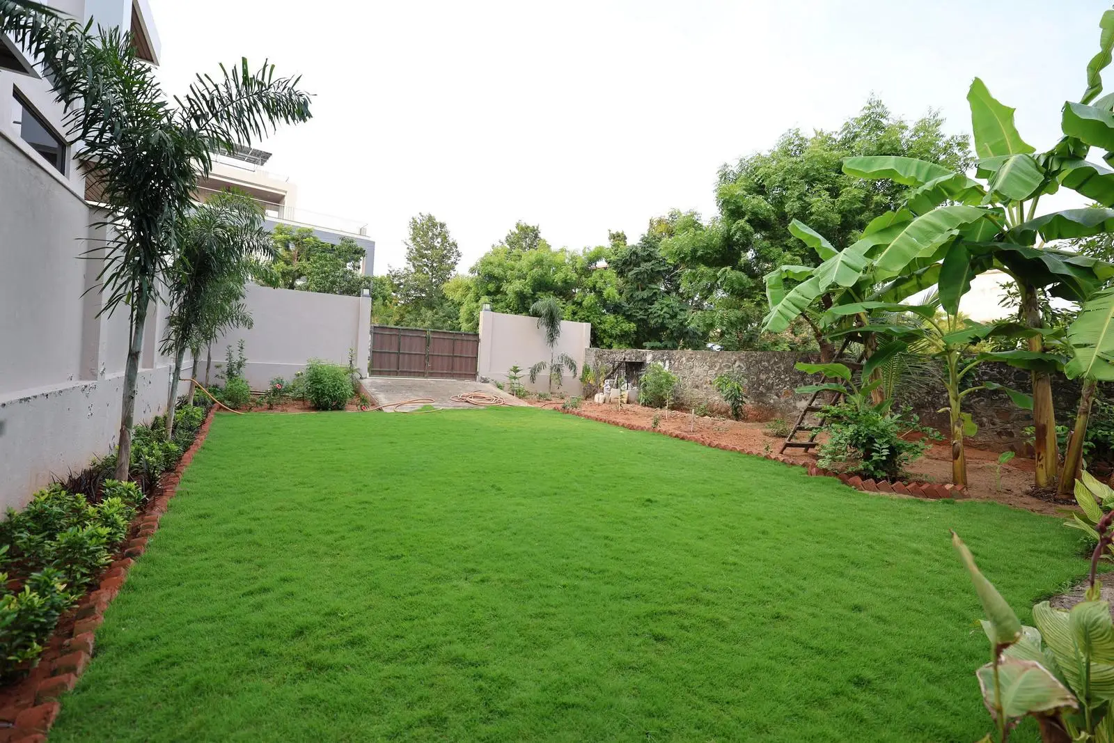 The courtyard is open and versatile, suitable for gatherings, play, or relaxation, with layered vegetation creating privacy. Subtle drainage, a gate, and driveway maintain functionality while preserving visual symmetry.