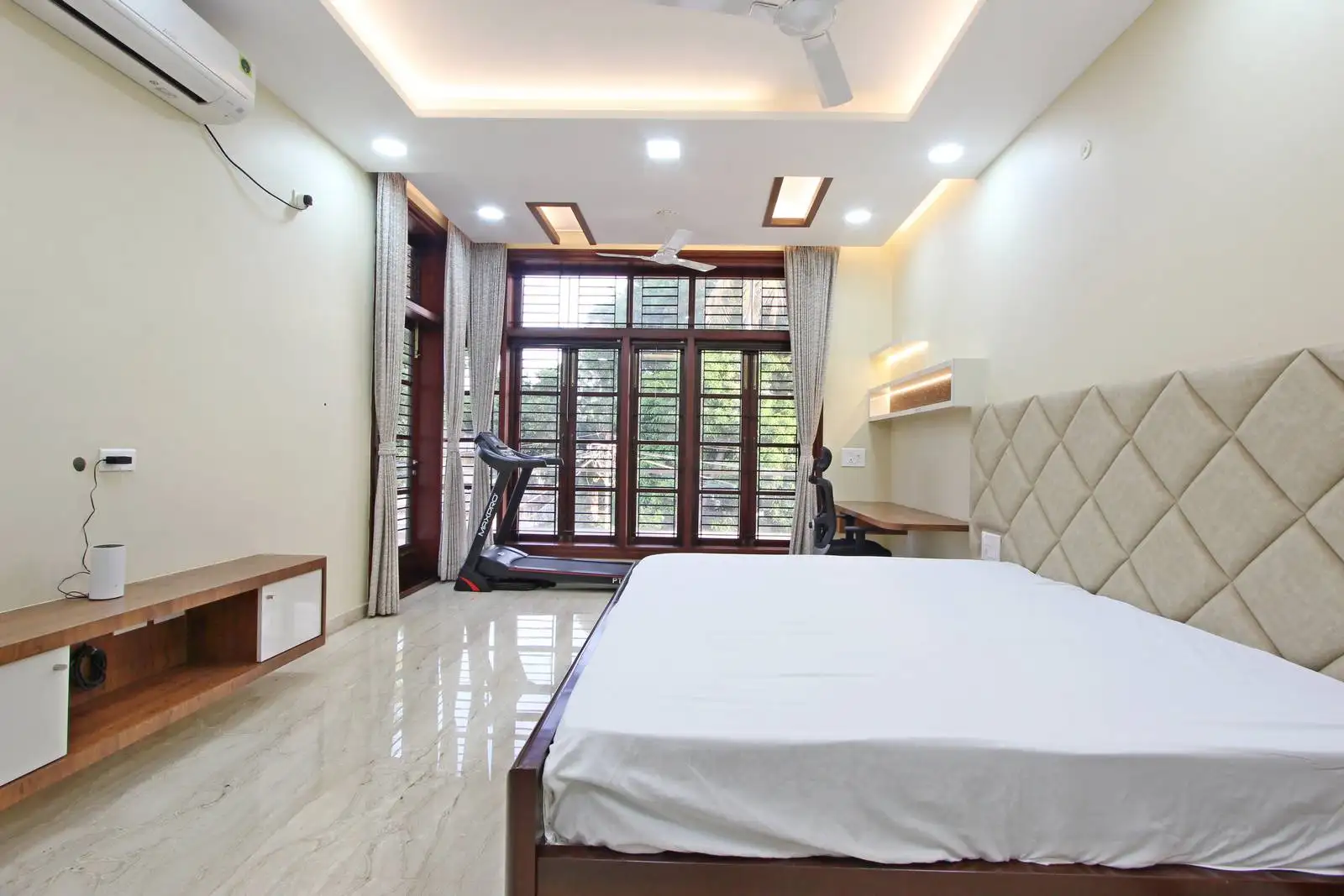 Multifunctional bedroom combining sleeping, working, and fitness areas, featuring a large window/door for natural light and balcony access, with integrated workspace and treadmill for productivity and wellness.