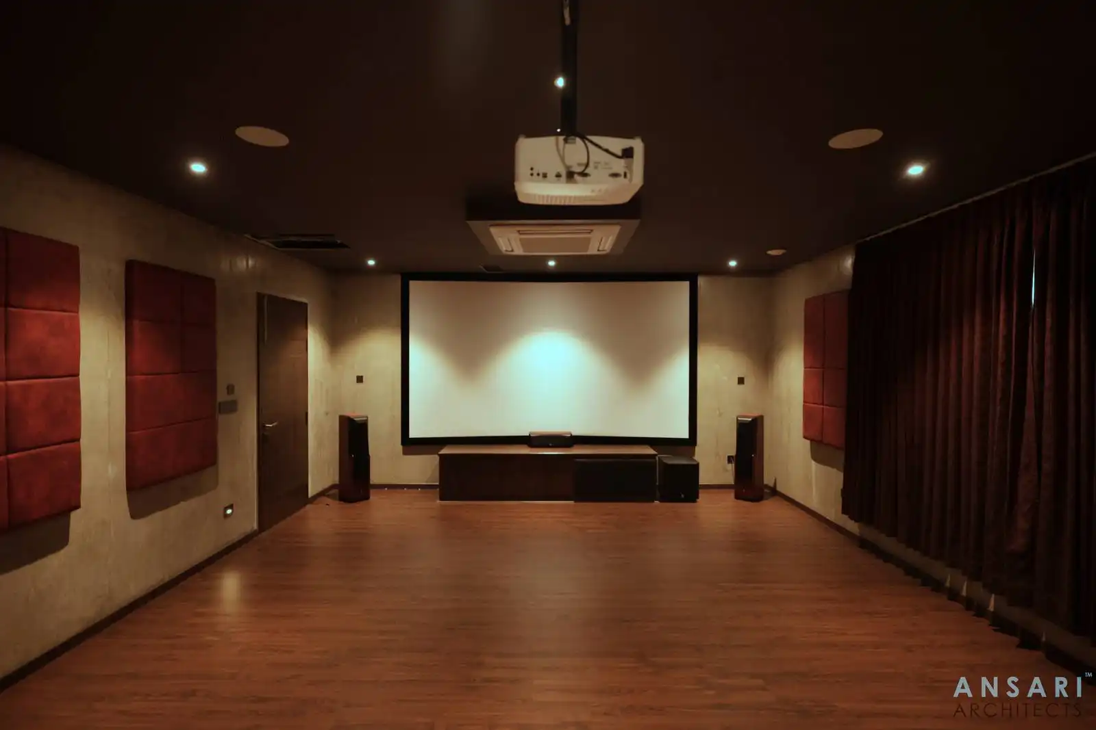 Home theater with red acoustic panel walls and integrated speakers for optimal sound clarity. Projection-ready layout with concealed ceiling mounts ensures a seamless cinematic experience.