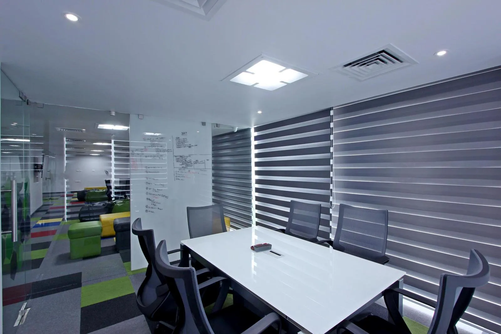 The conference room features a white high-gloss table with ergonomic chairs, modular carpet, and a glass writing wall for collaborative sessions. Dual-tone blinds, recessed LED lighting, and glass partitions enhance comfort, privacy, and visual connectivity.