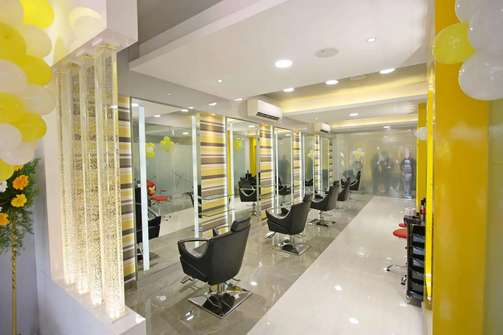 The salon combines bold colors, reflective surfaces, and modern finishes to create a bright, welcoming, and professional environment. Key design elements frameless glass entrance, patterned laminated walls, ergonomic stations, and illuminated glass partitions enhance visual appeal, functionality, and spatial flow.