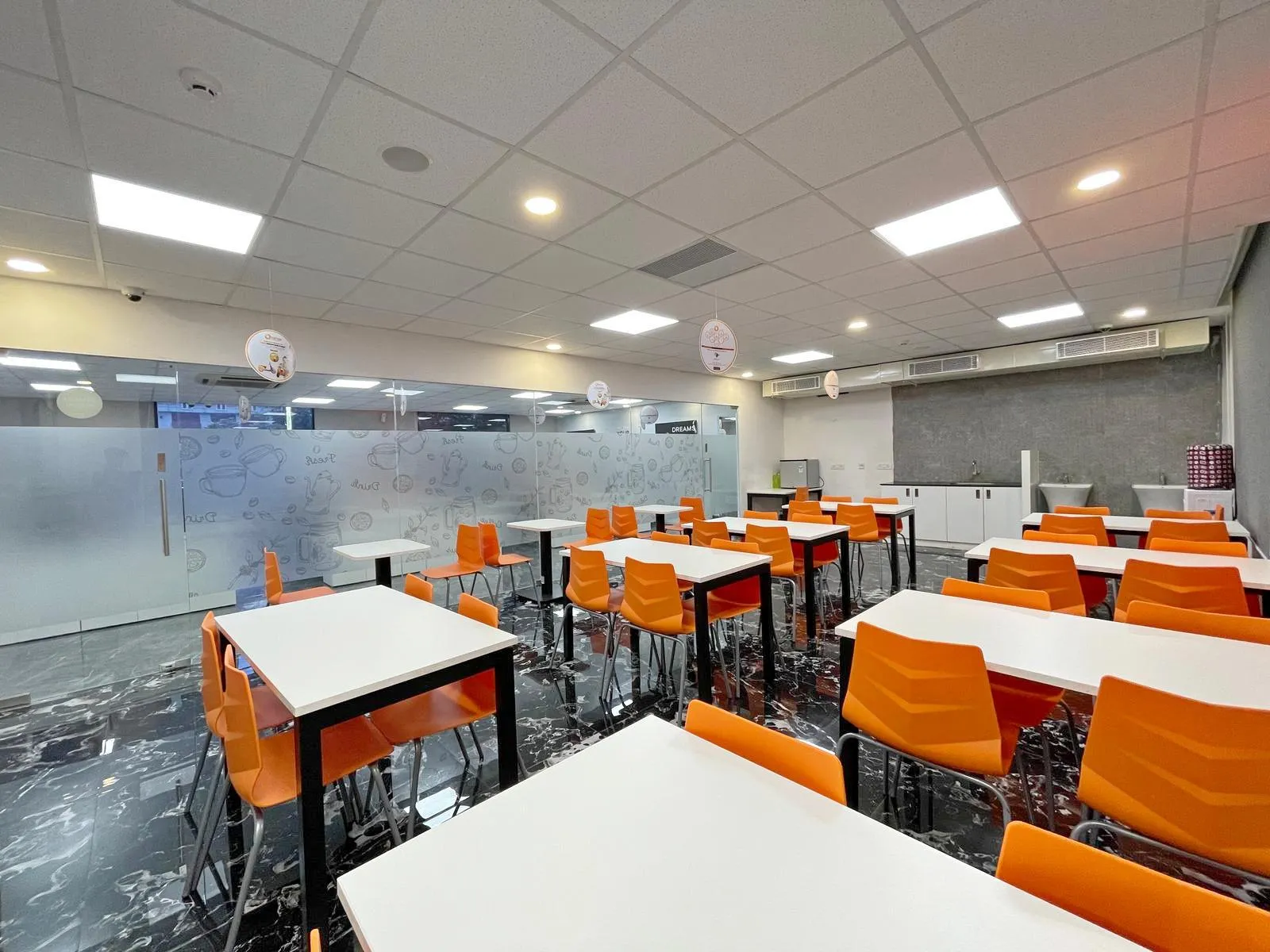 The 42-seater cafeteria and training room features a modular layout with vibrant seating and flexible tables, supporting both dining and collaborative activities. Polished floors, acoustic ceilings, and integrated storage ensure a functional, organized, and visually appealing environment.