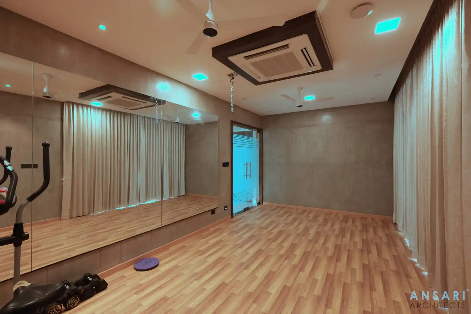 Spacious room with warm wooden floors, floor-to-ceiling mirrors, and large windows. Neutral tones and minimalist design create a calm, functional space ideal for fitness, dance, or relaxation.