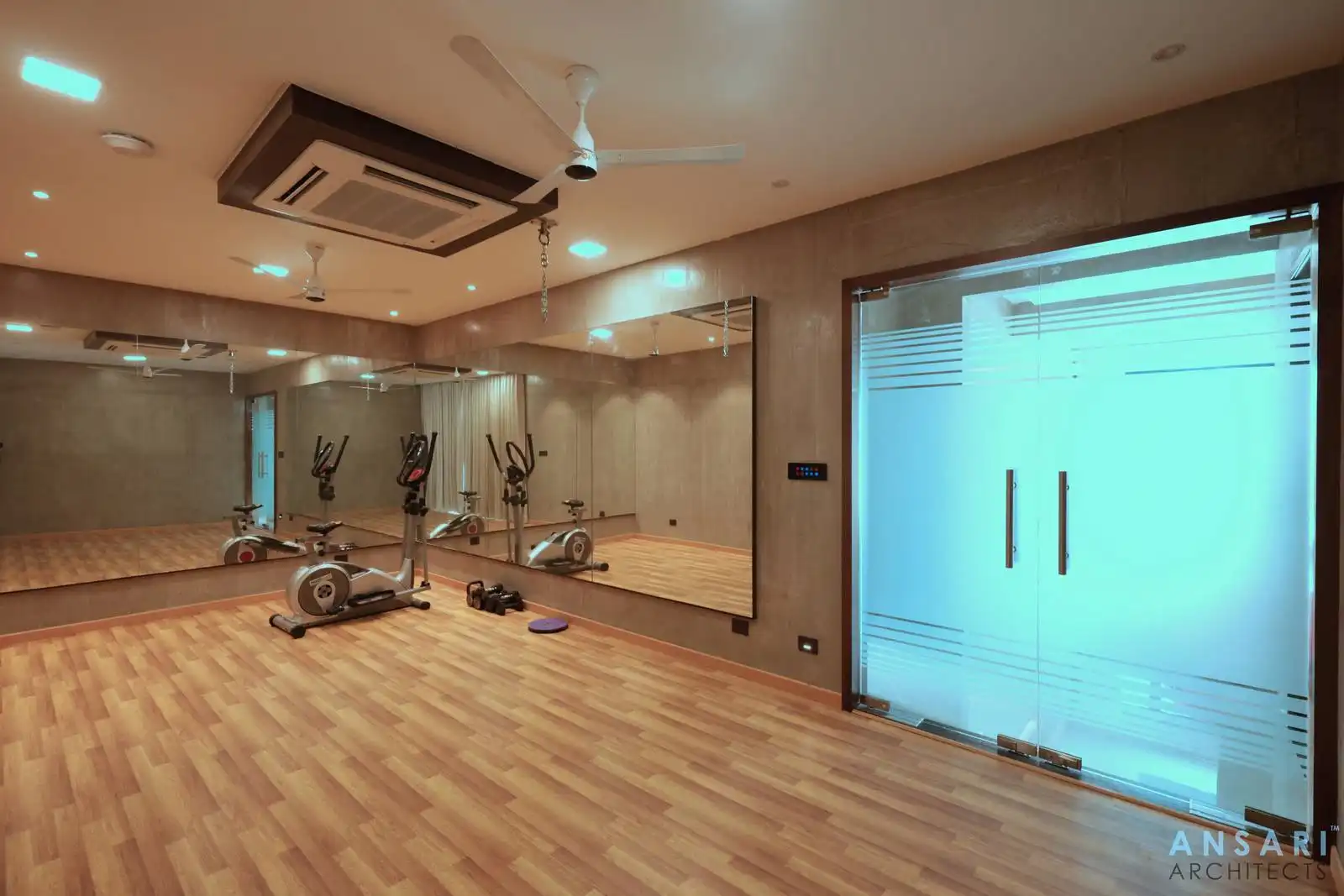 Multipurpose room for dance, gym, and yoga featuring a mirrored wall, wooden flooring, textured finishes, and a frosted glass partition for privacy.
