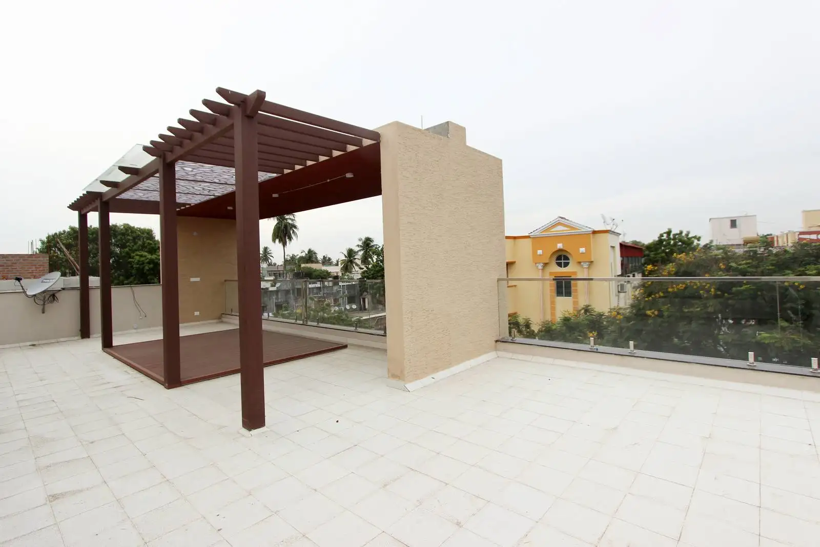 Designed terrace features a raised wooden deck beneath a sleek brown pergola, set against a clean white tiled floor. 