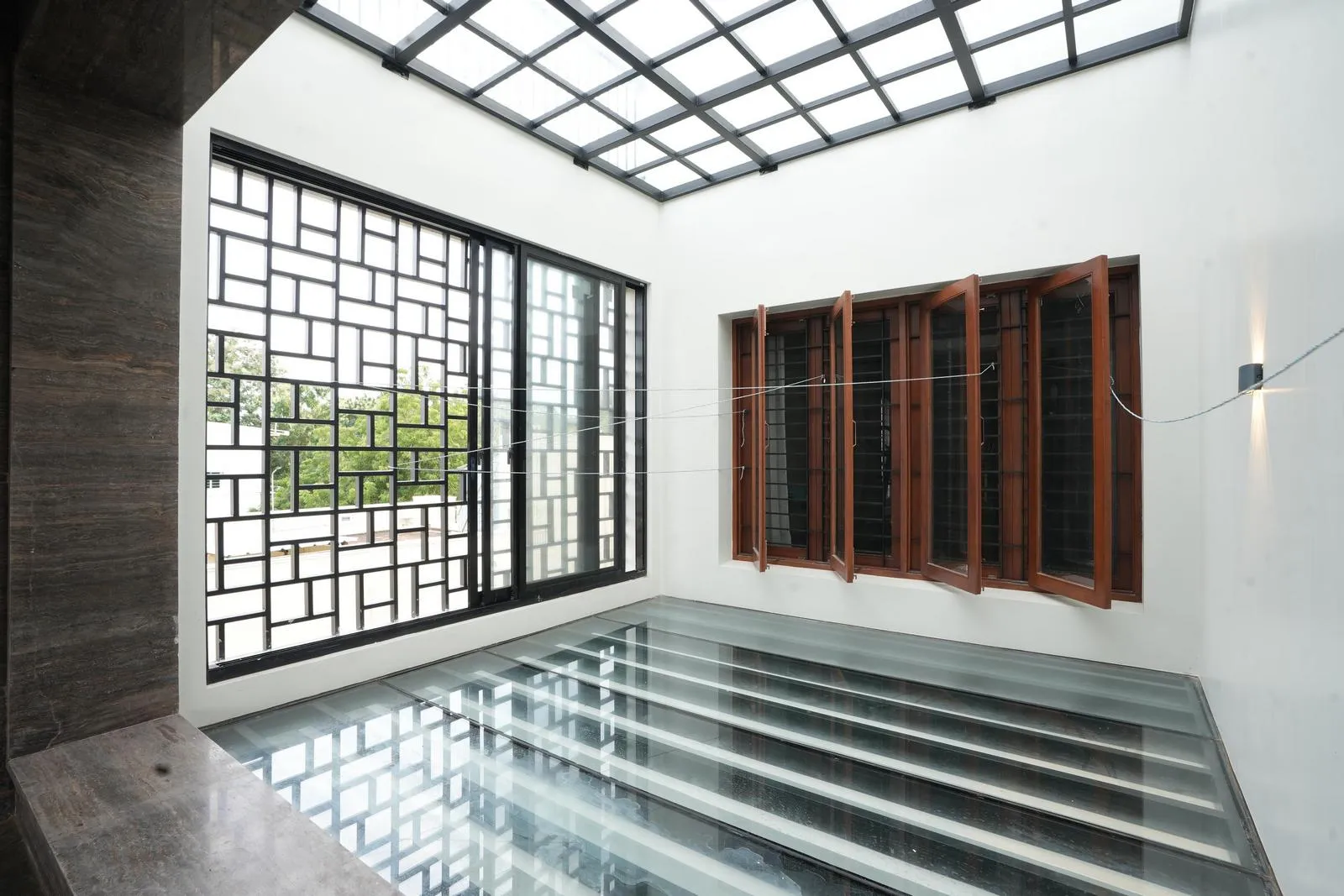 A semi-open transitional space connects indoor and outdoor environments. A pergola roof filters sunlight, while glass flooring enhances openness and visual depth, creating a dynamic play of light and shadow.