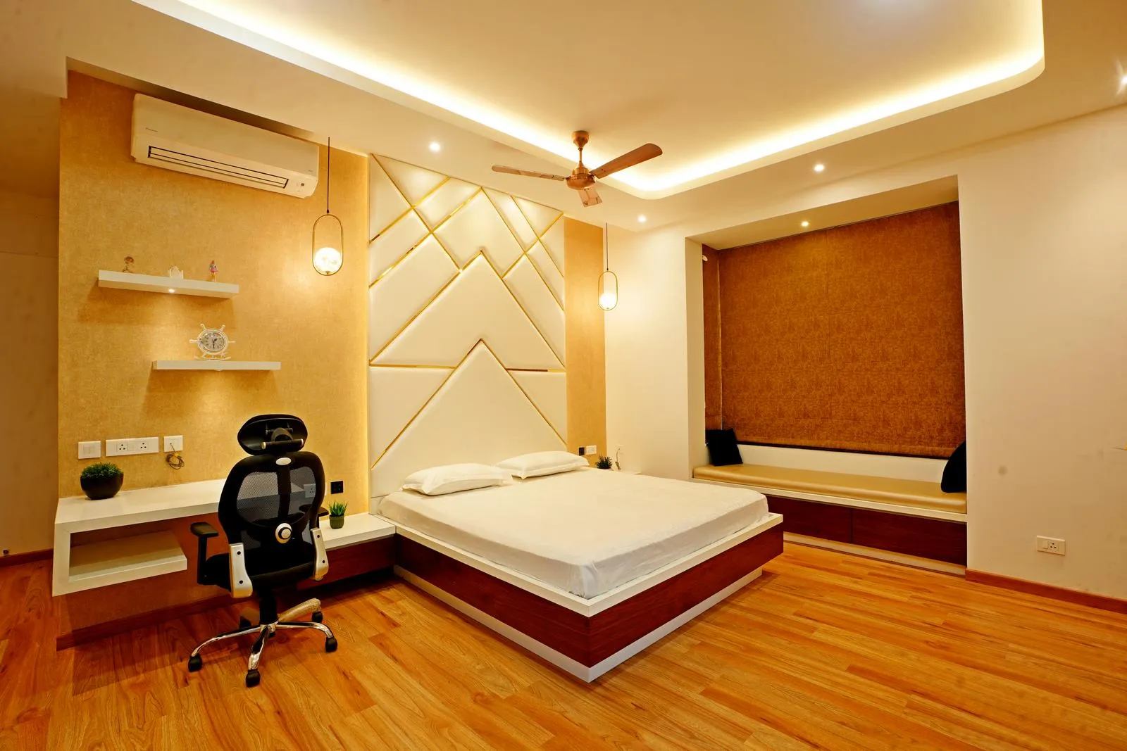 The bedroom (18'0" x 14'0") is symmetrically designed with a central bed, integrated study desk, and window seating nook for balanced functionality. Warm beige walls, natural wood flooring, and a padded beige leatherette headboard create a cozy, modern, and elegant space.