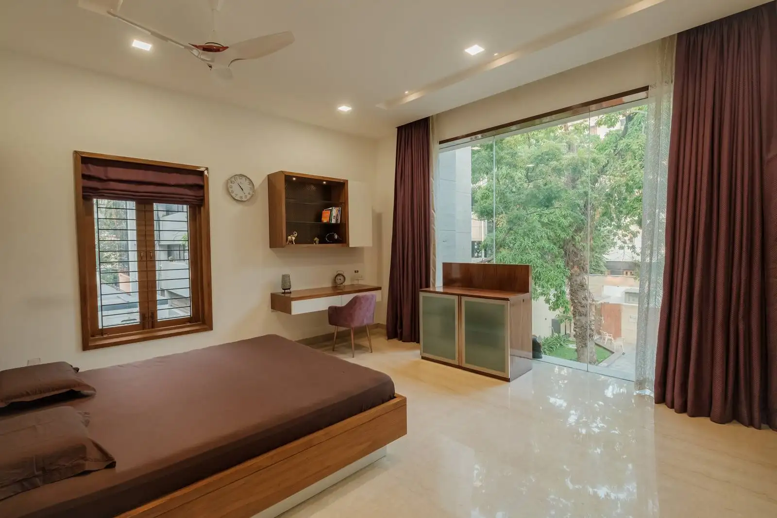 A large wood-framed glass window with full-length curtains enhances privacy while connecting the bedroom to the courtyard, promoting seamless indoor-outdoor living.