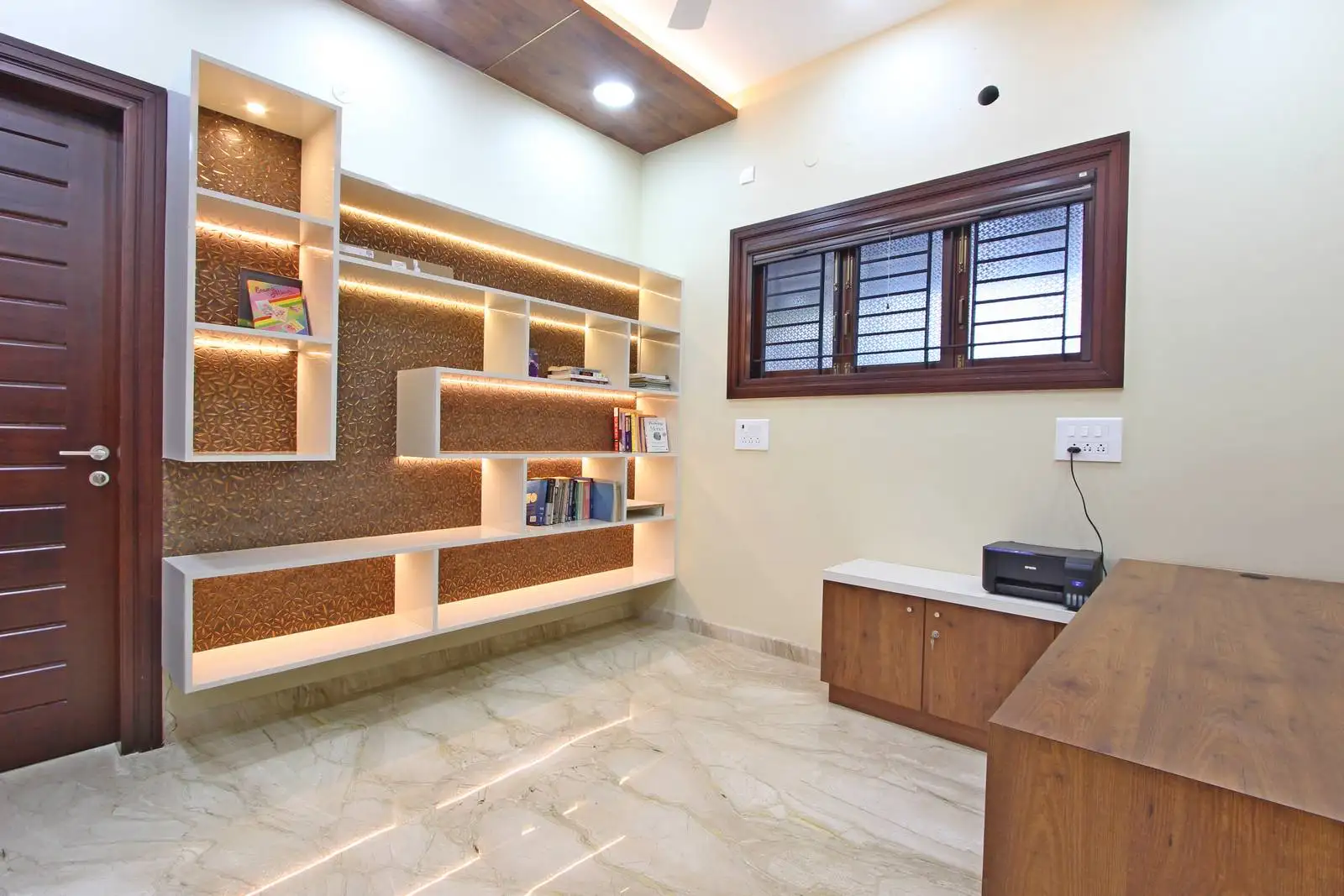 A compact, well-organized study room with a wall-mounted desk and full-length shelving unit, providing ample workspace, storage, and display space in an efficient layout.