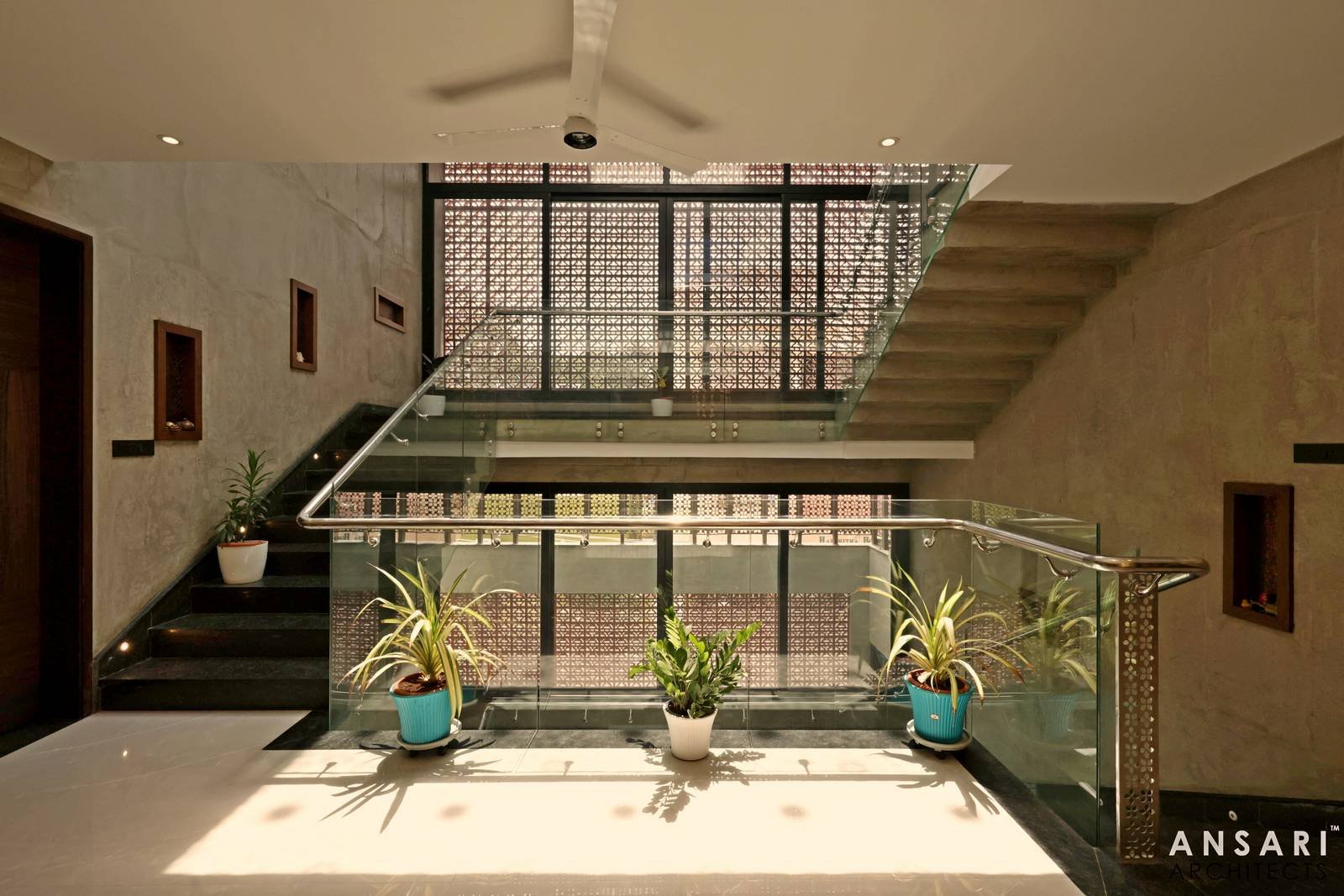 Indoor staircase features sleek glass railings, metal handrails, and decorative screens that enhance privacy and light play, complemented by natural greenery.
