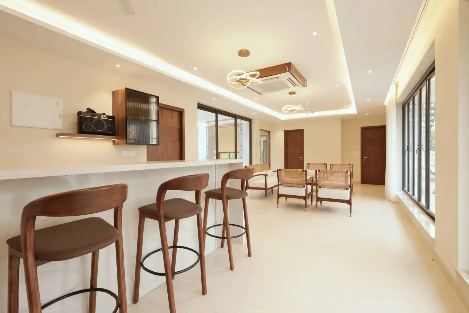 An open and elongated third-floor multipurpose lounge featuring a long bar counter, cozy seating area, and full-height glass windows that open to a terrace, creating a bright and inviting social space.