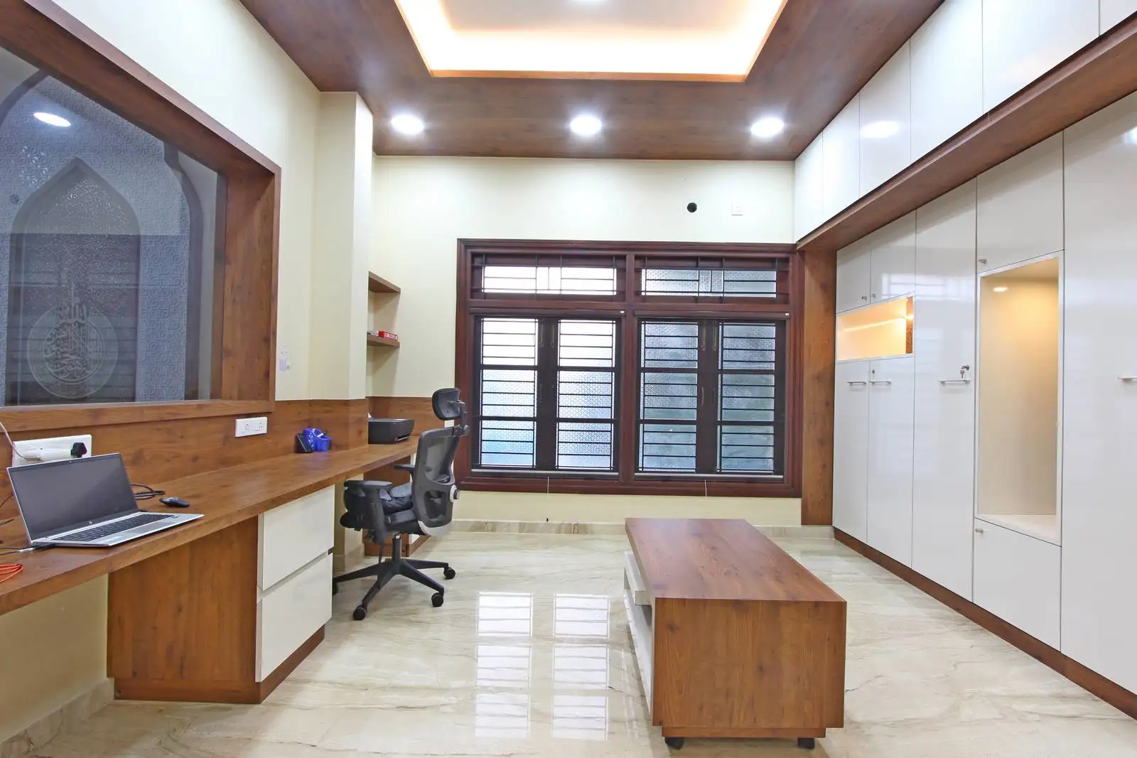 Large framed windows at the back bring in abundant natural light and outdoor views, boosting productivity and well-being. White built-in cabinets with wooden accents along the side wall provide generous storage, keeping the office organized and clutter-free.