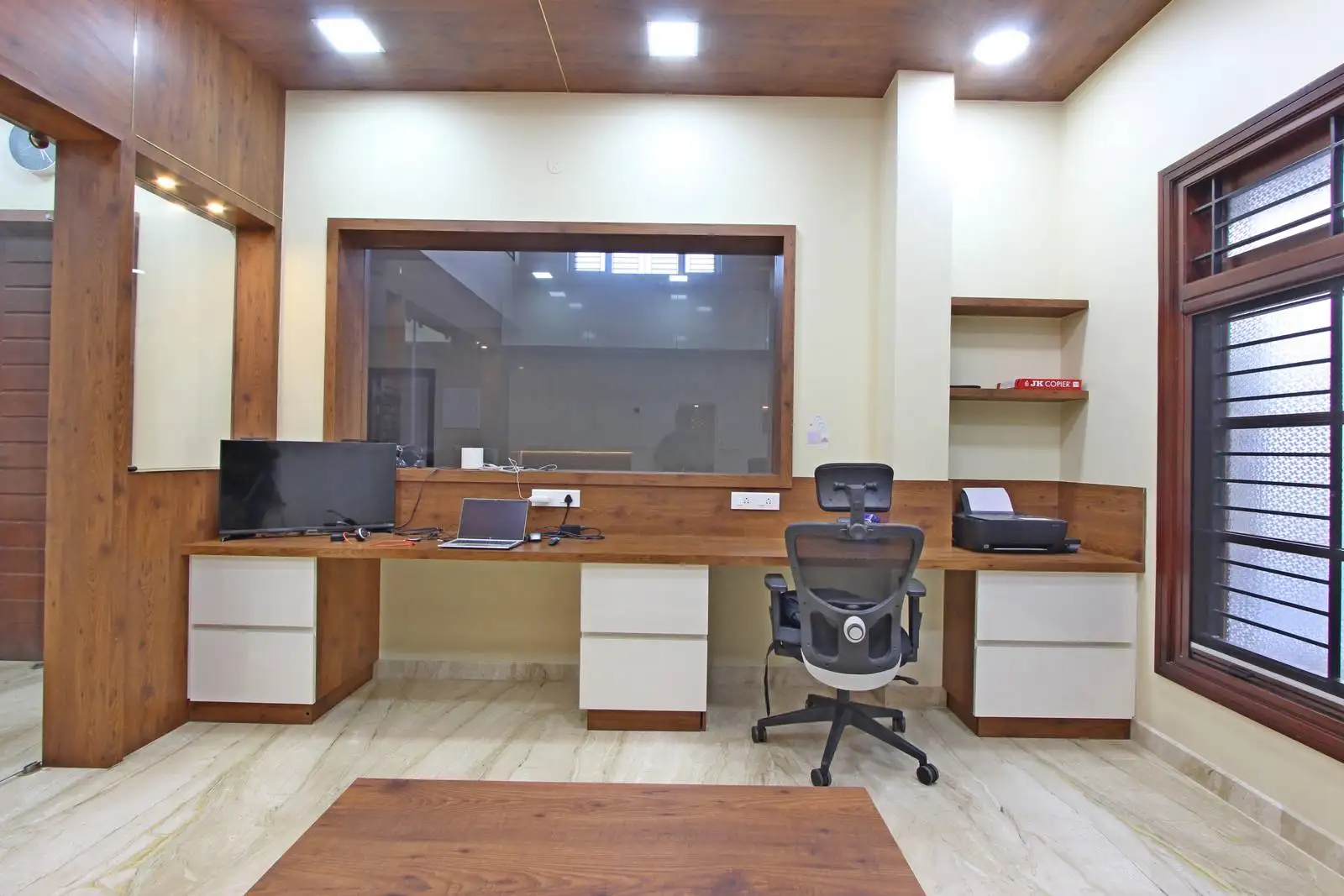 A functional and well-lit office workspace featuring a full-length wooden desk, ergonomic seating, ample storage, and a large window for natural light—designed to blend productivity with modern aesthetics.