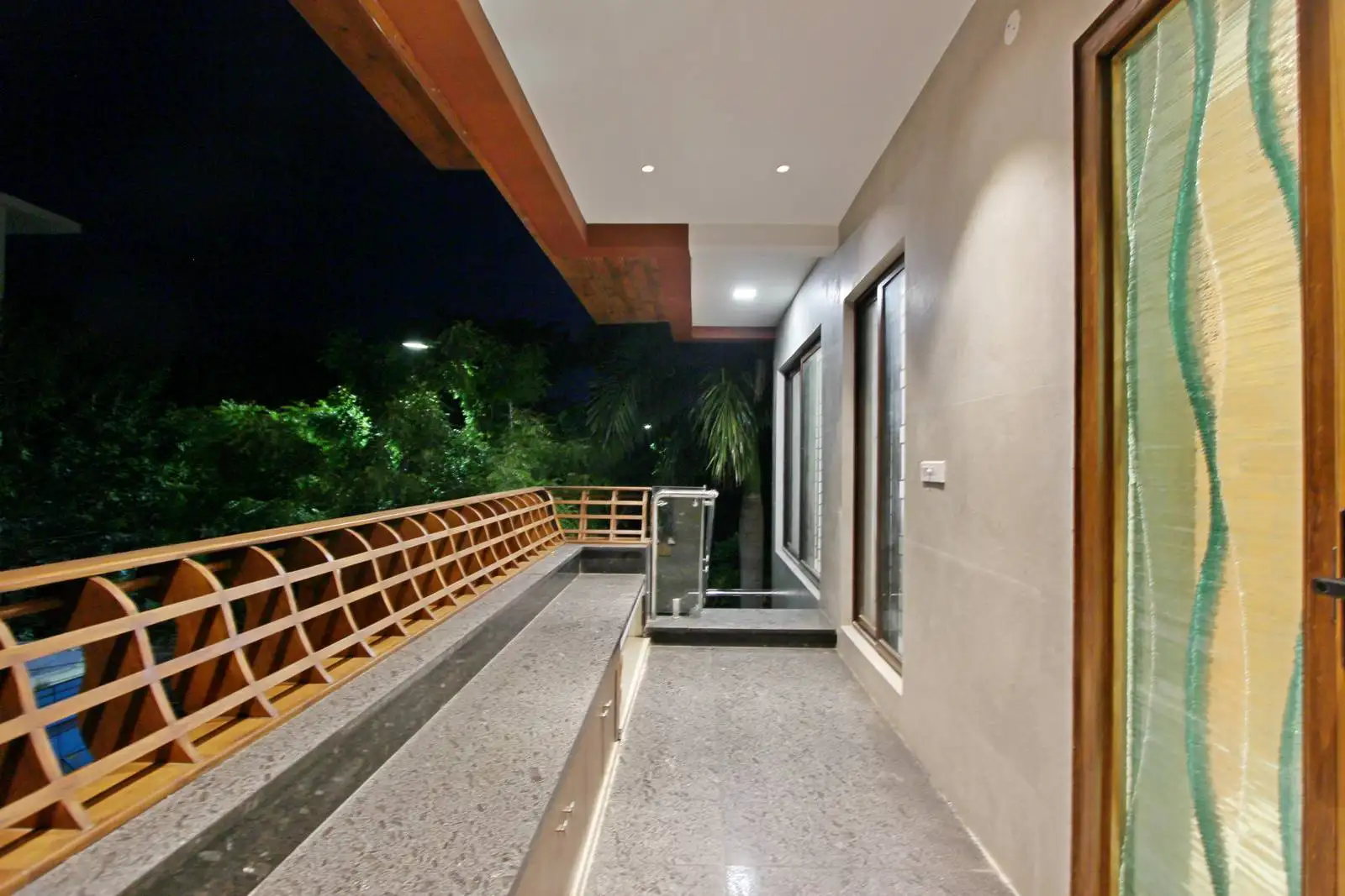 The verandah is a long, narrow outdoor space adjacent to the main building, accessible through a glass door with a metal grill for security and aesthetics.