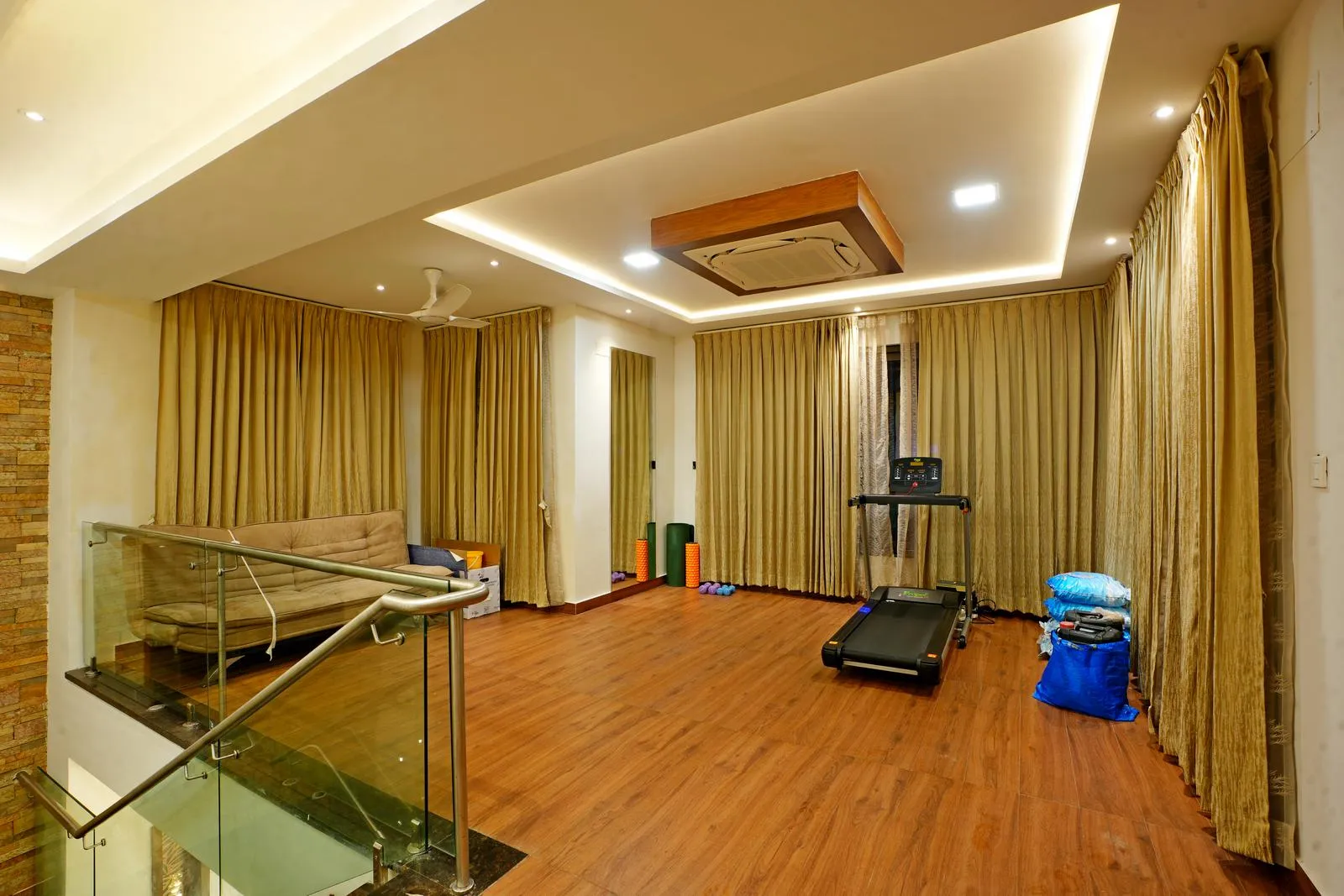 The 20'0" x 22'0" gym room on the second floor combines a fitness zone with a casual lounge, offering flexibility for workouts and relaxation. Warm wooden flooring, neutral walls, and glass railings create an open, bright, and inviting space.