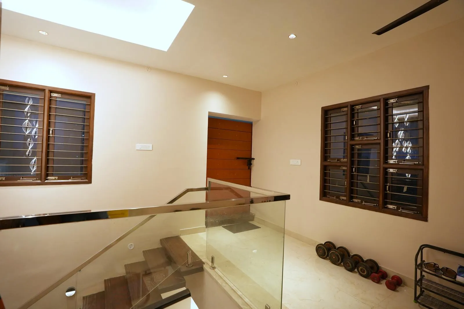 Lift Lobby ( 10'6" x 14'2" sq.ft ) is designed as a bright transitional space connecting the lift and staircase, with a glass-railed stair void enhancing openness and light flow. Cream marble flooring and warm wooden accents reinforce a clean, contemporary architectural character.