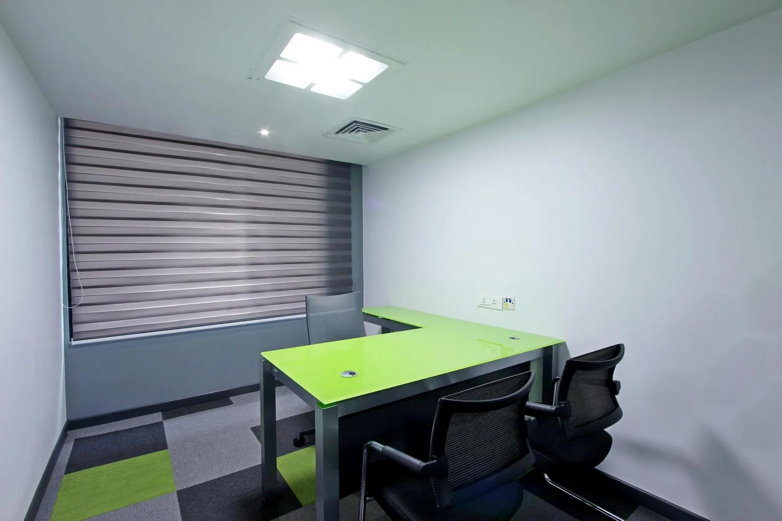 The executive cabin features a lime green laminated desk with ergonomic seating, modular carpet, and recessed LED lighting, creating a bright, functional, and professional workspace. Dual-tone blinds and integrated air-conditioning enhance comfort, privacy, and visual harmony.