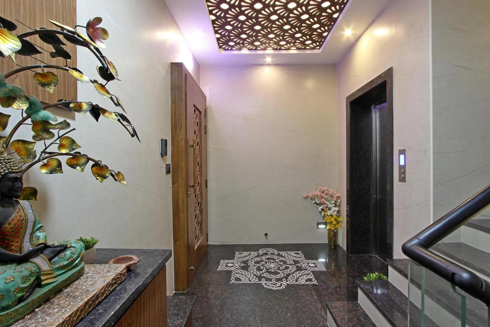 The first-floor lift lobby features polished black granite flooring, marble-textured walls, warm wooden accents, and a decorative console with artistic and spiritual details.