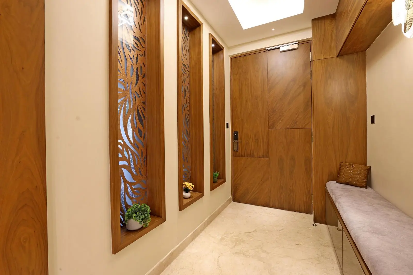 The foyer welcomes visitors with a rectilinear layout leading to the main living area. Warm wood finishes, marble flooring, and frosted glass panels create a sophisticated, inviting palette. Built-in seating, decorative niches, and layered lighting balance functionality with modern architectural detailing.