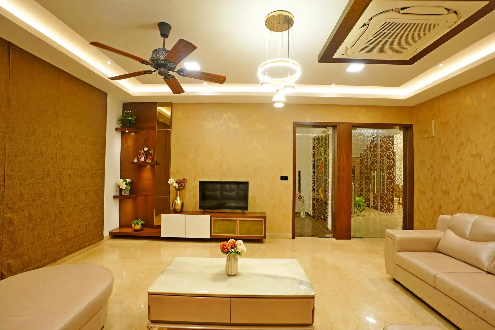 The living room is centered around a TV wall, creating a cohesive focal point. The open layout and glass-paneled doorway ensure smooth circulation and visual connectivity with adjoining spaces.