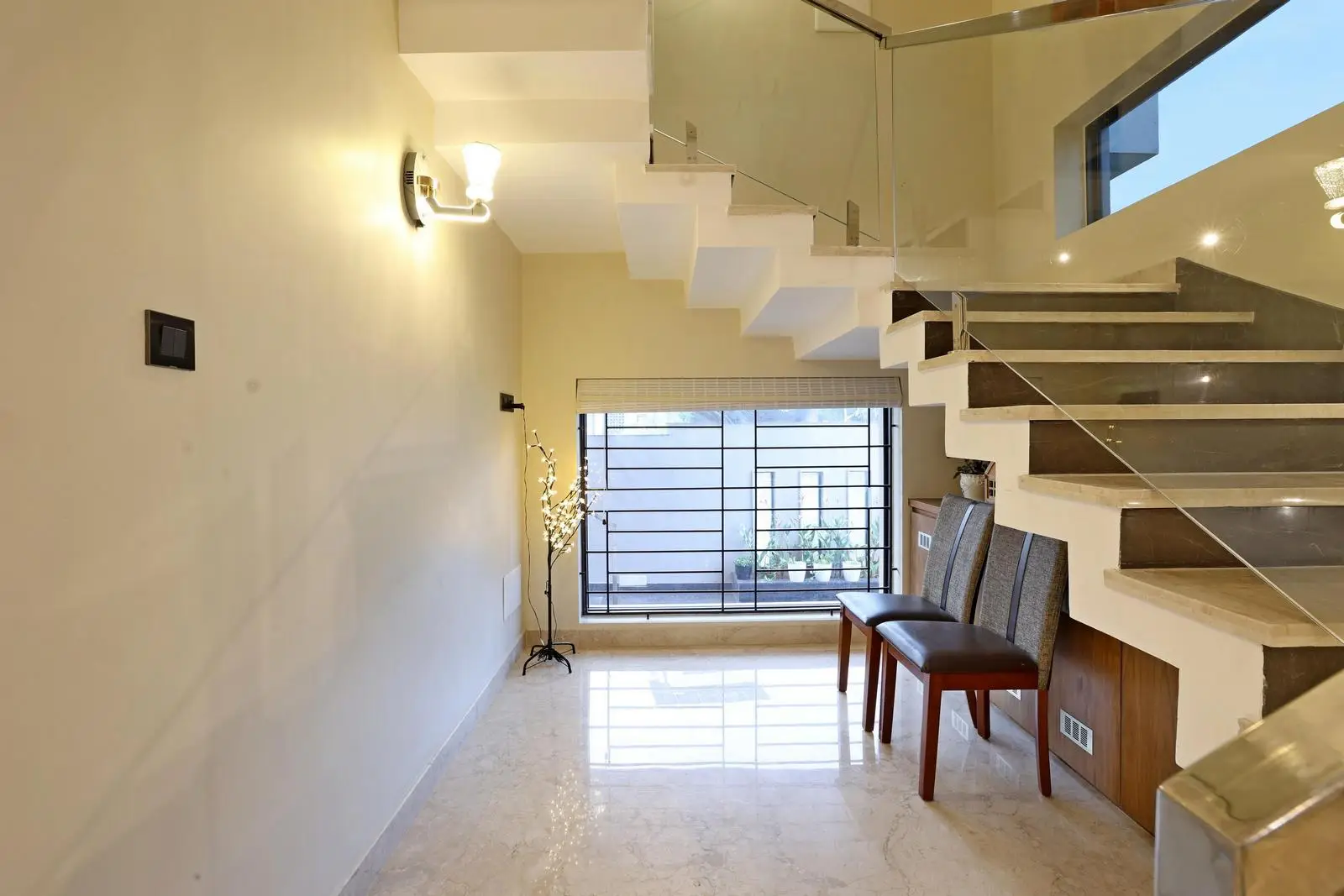 The utility area beneath the staircase efficiently transforms underused space into a functional seating and storage zone. A linear layout and end window maintain openness, natural light, and smooth circulation.