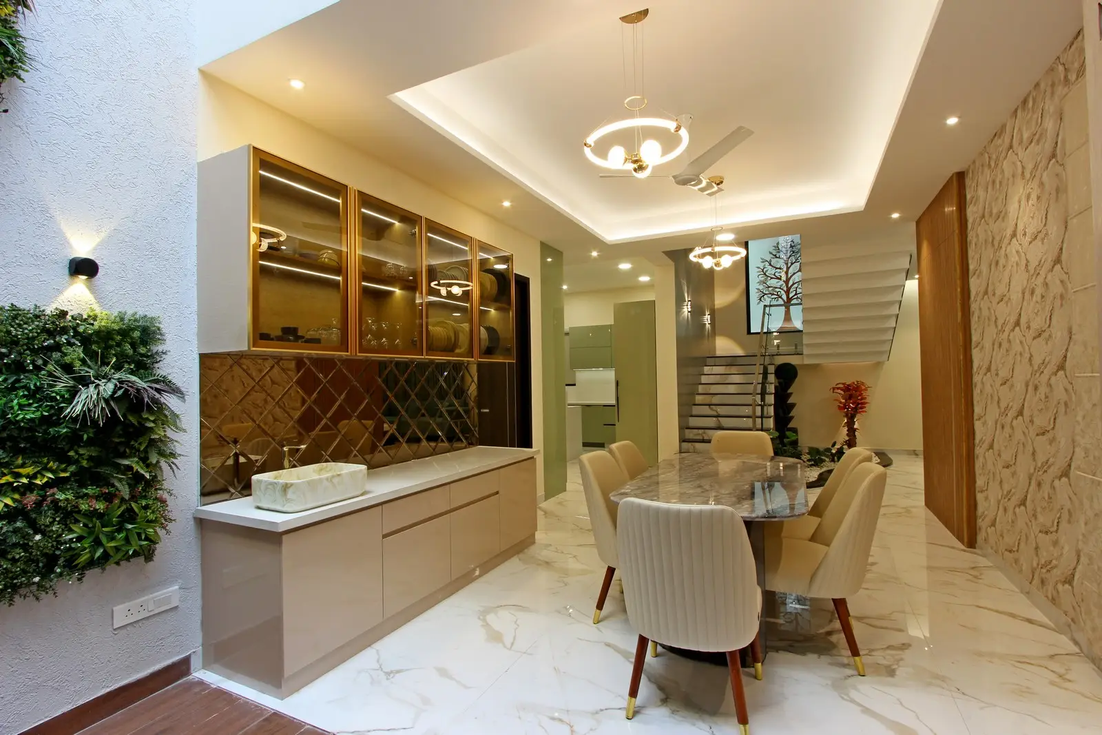 Enhancing the interior’s sophistication, recessed ceiling lights and modern chandeliers illuminate the area, while a built-in cabinet with glass shelves and gold accents adds both style and practicality.