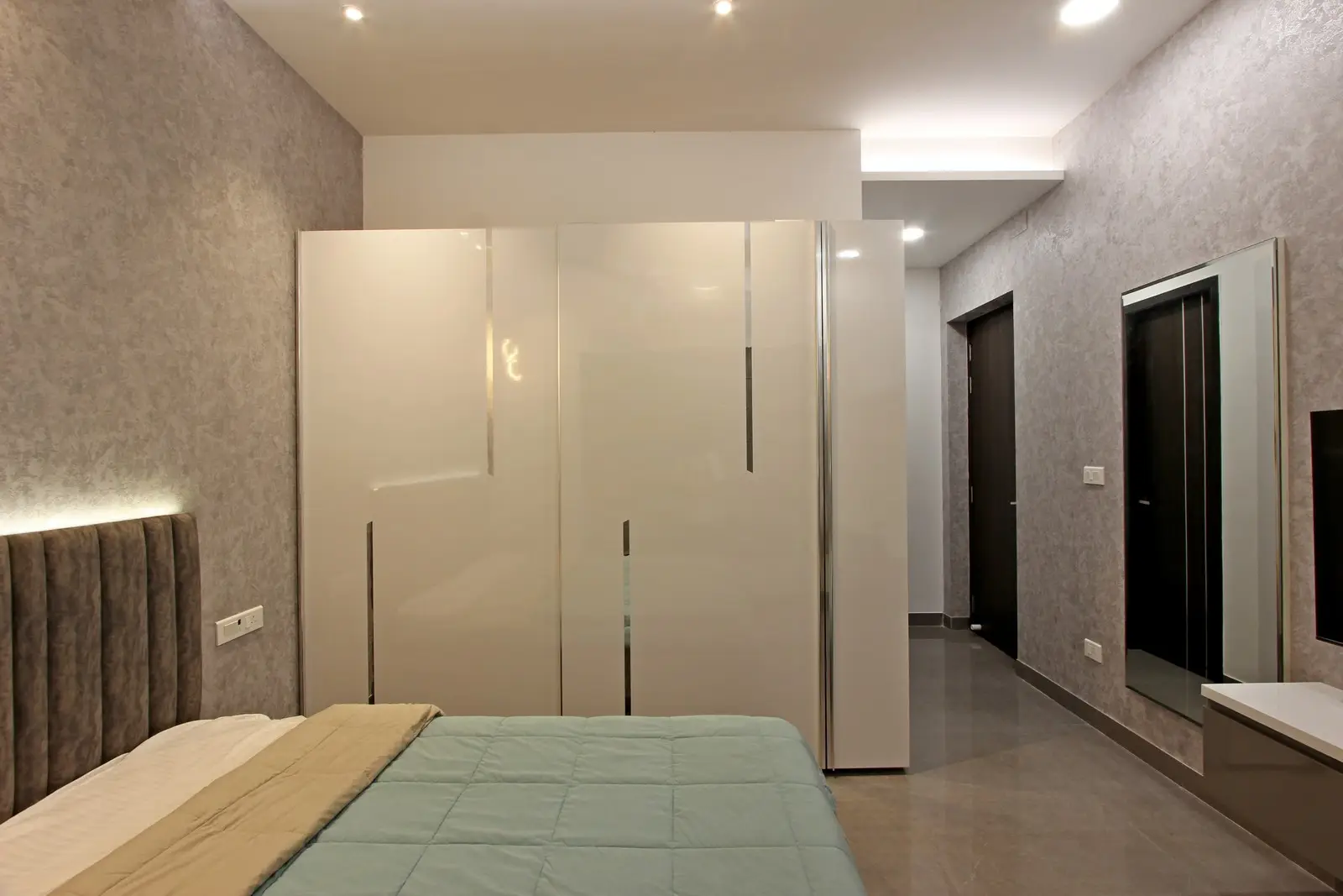 Glossy white wardrobes and light wooden flooring reflect natural light, contributing to the room's spacious and serene environment.
