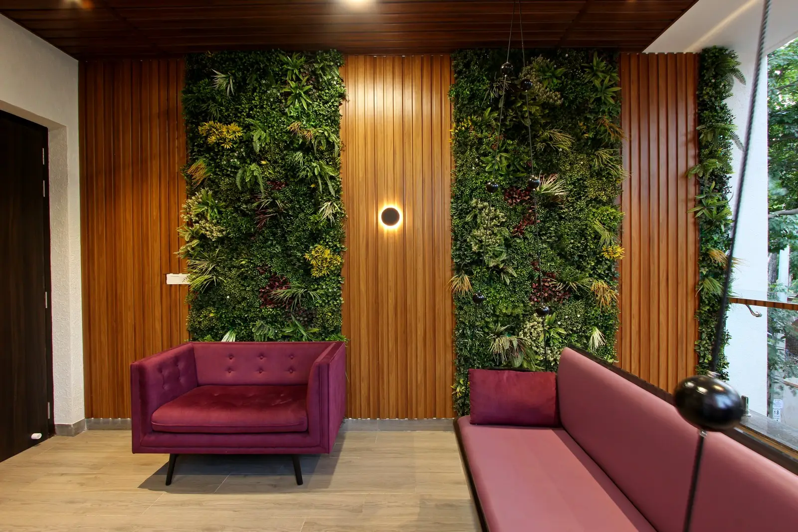 Lush green walls, vertical wooden panels, maroon seating, and warm lighting come together to create a serene, stylish, and contemporary lounge atmosphere.
