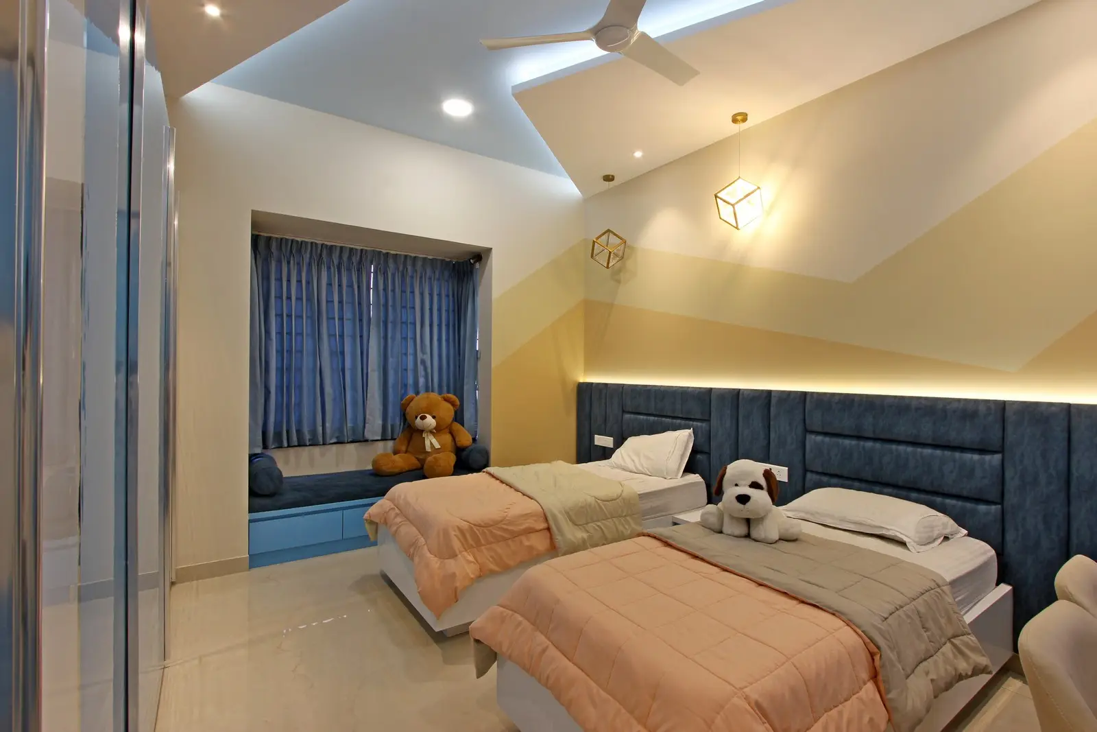 A golden pendant lights and a blue study nook add elegance and function, while soft bedding and subtle lighting create a cozy, modern atmosphere.

