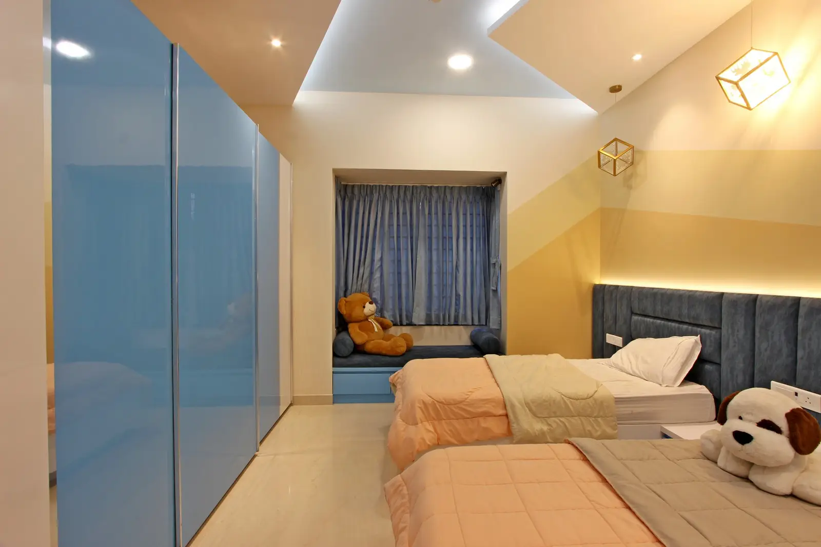 The deep blue headboard with concealed LED lighting adds warmth, while beige, cream, and pastel geometric wall patterns create a playful yet balanced atmosphere.
