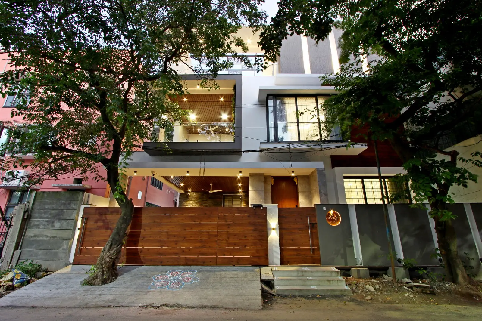 Contemporary residence features layered balconies with recessed lighting, sleek glass railings, and a grand wooden gate, blending modern architecture with natural surroundings beautifully.