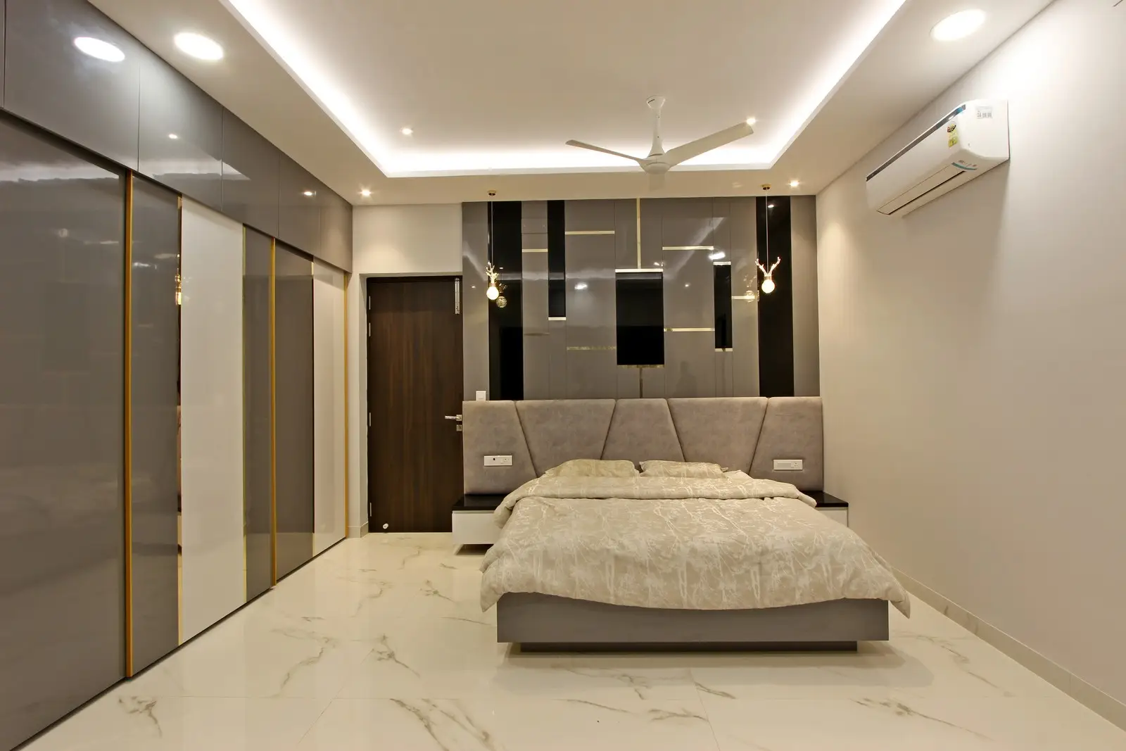 This elegant bedroom features a grey upholstered bed, glossy black and grey wall panels, marble flooring, and recessed lighting, creating a luxurious modern ambiance.