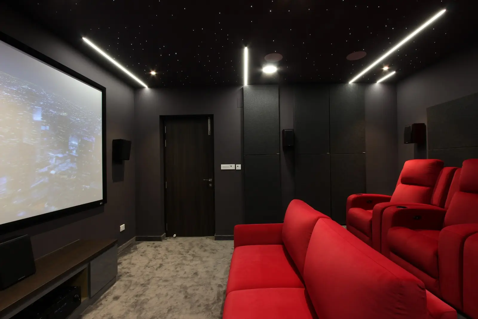 This luxurious home theater features matte charcoal walls with acoustic panels, red recliners, starry ceiling lights, and a large projection screen for a cinematic experience.

