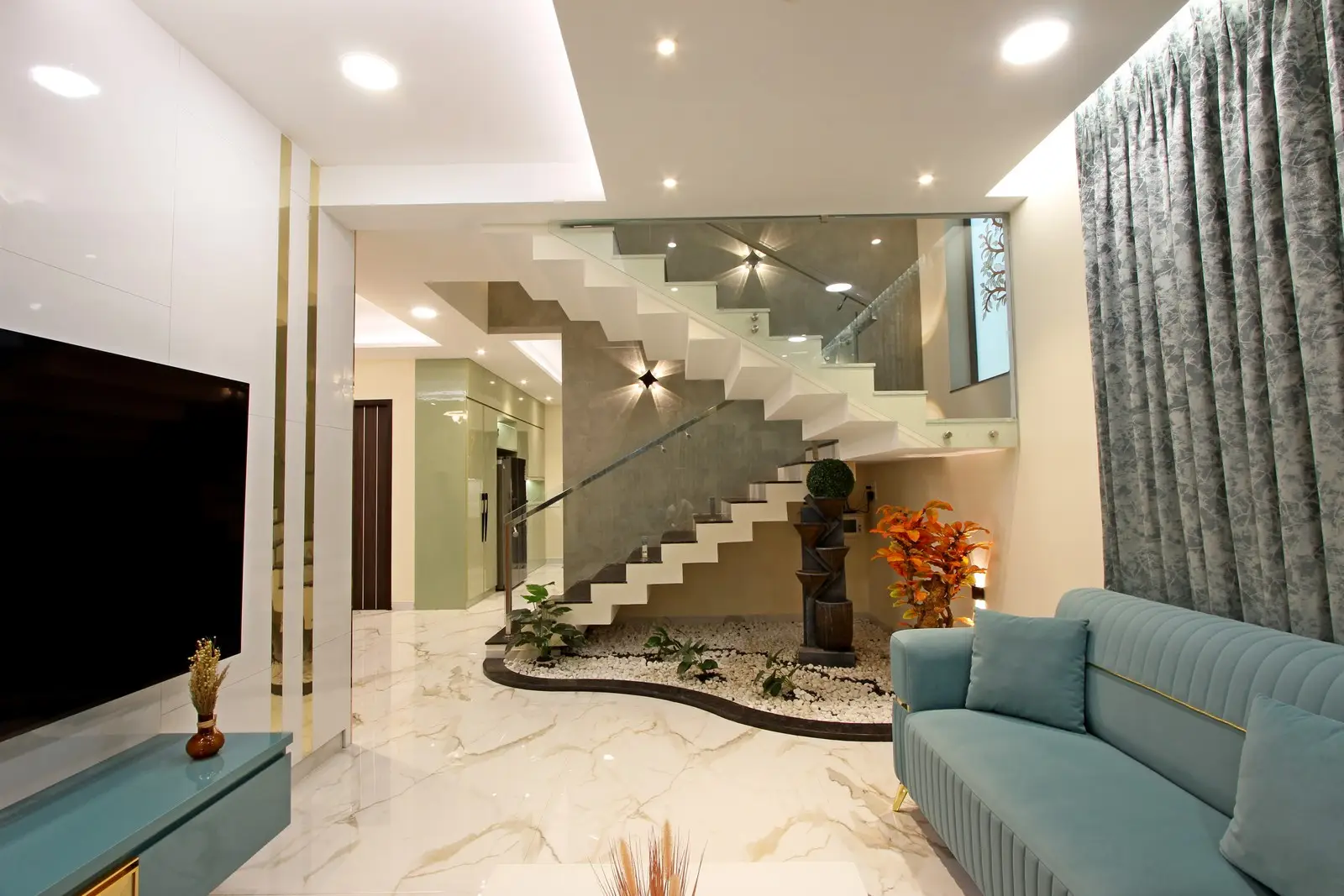 A floating staircase with glass railings, marble flooring, elegant teal seating, and ambient lighting, creating a sophisticated and spacious atmosphere.
