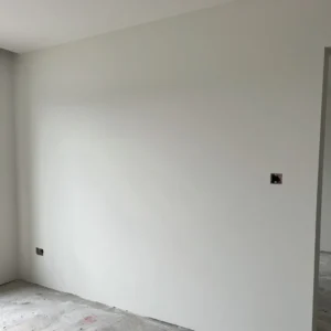 How to Stop Cracks in Your Home: Professional Guidance from Architect Dameem Ansari 6 Unfinished interior room with white plastered walls, two small rectangular electrical outlet openings, and a bare concrete floor showing signs of construction work.