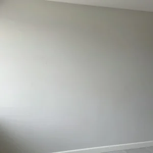 How to Stop Cracks in Your Home: Professional Guidance from Architect Dameem Ansari 10 Light gray interior wall with faint cracks visible, white baseboard at the bottom, and tiled floor partially visible.