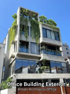 Modern office building with large glass windows and concrete exterior, adorned with hanging plants and greenery on the balconies and rooftop against a clear blue sky