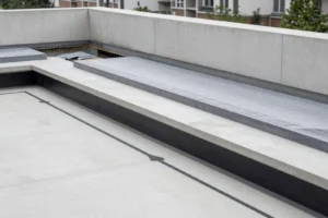 Empty modern outdoor concrete seating area with a backrest wall and layered concrete bench surfaces surrounded by a low wall, with some trees and buildings in the background.