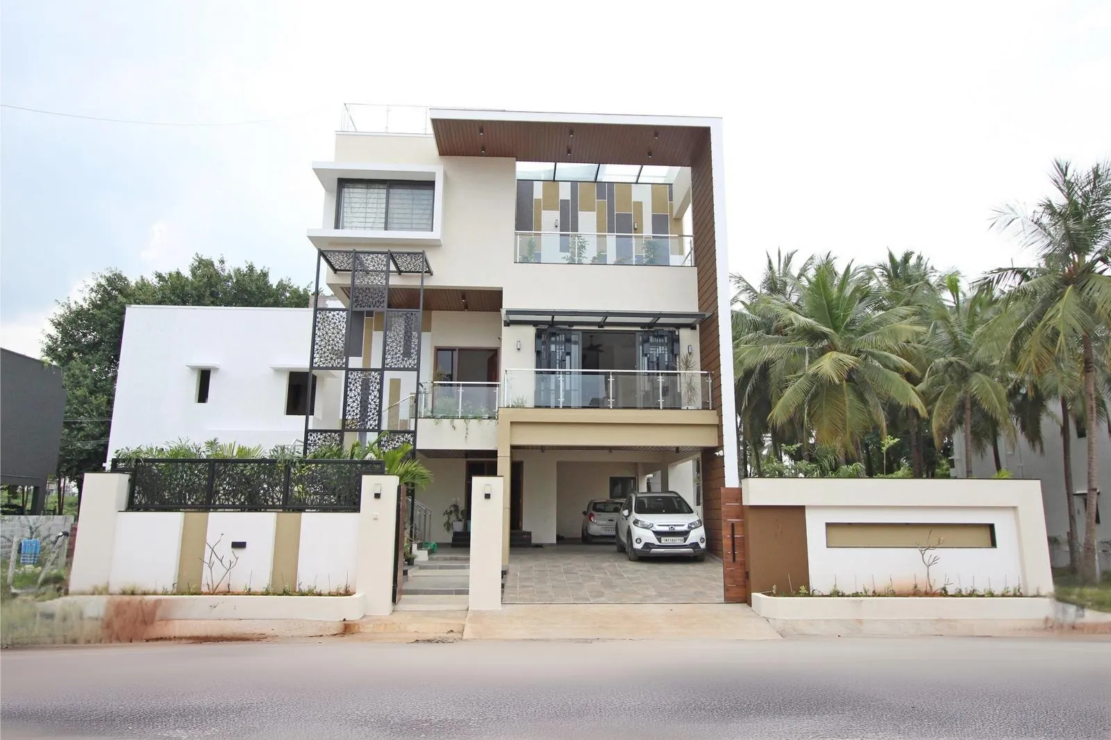 The facade mixes white plaster, wood finishes, and grey metal for a warm, modern look. Cantilevered roof frames, glass railings, and metal screens add depth, shade, and visual lightness to the street-facing design.