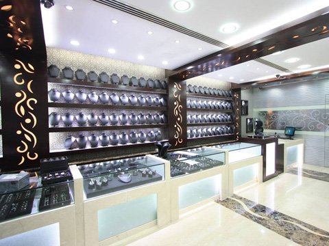 Interior of a well-lit jewelry store with multiple illuminated display cases filled with jewelry and necklace stands arranged on wall shelves.