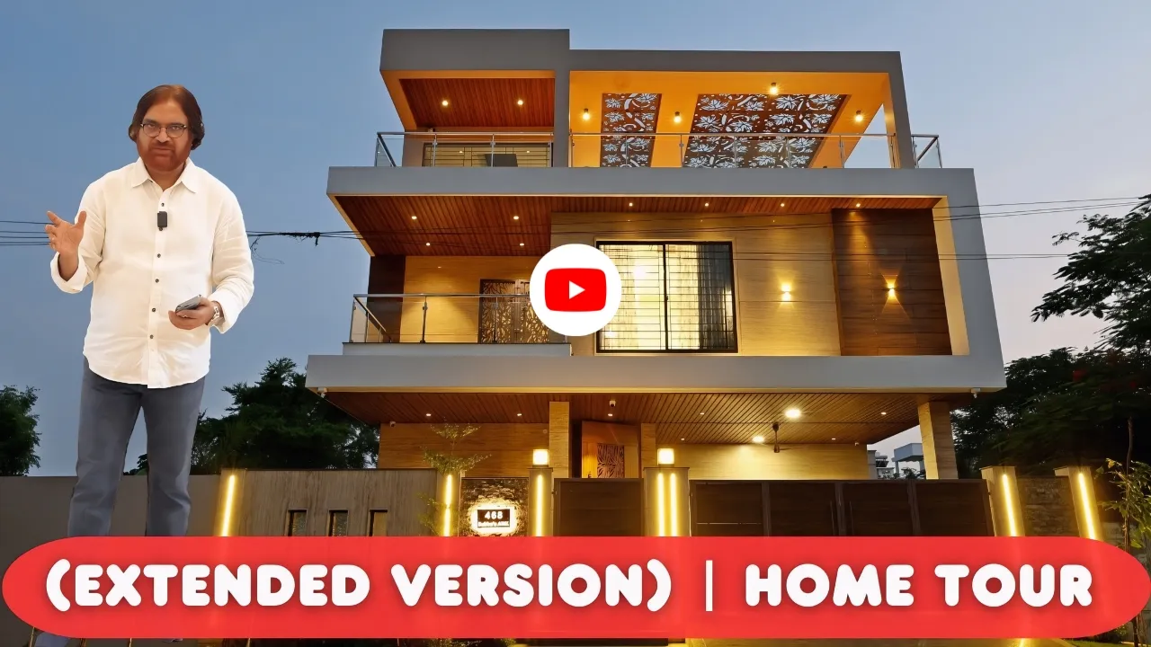Man in white shirt and gray pants standing in front of a modern two-story house with illuminated exterior and large windows at dusk, with text overlay reading '(EXTENDED VERSION) | HOME TOUR'