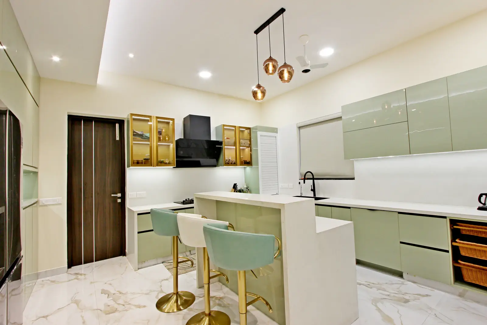 A stylish breakfast counter with a waterfall edge showcases mint green and cream bar stools, copper pendant lights, and marble flooring that enhance warmth and elegance.

