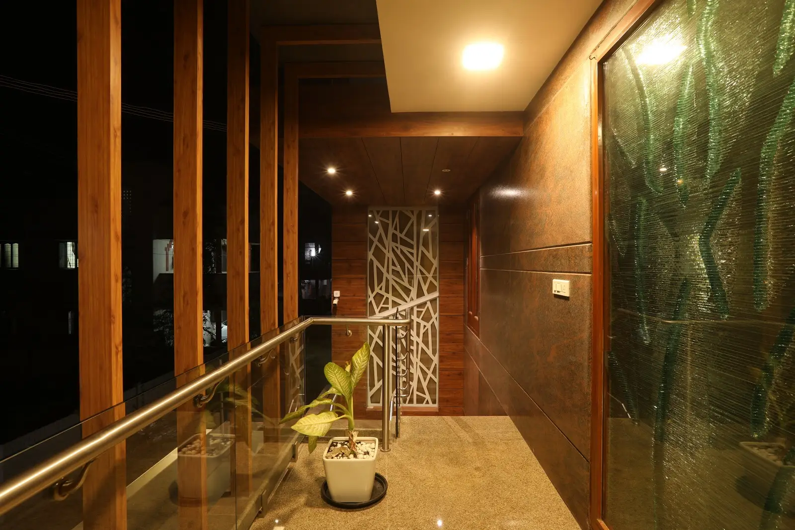 The first-floor - balcony features warm lighting, wooden paneling, glass railings, and potted plants, creating a cozy, elegant, and contemporary outdoor walkway ambiance.