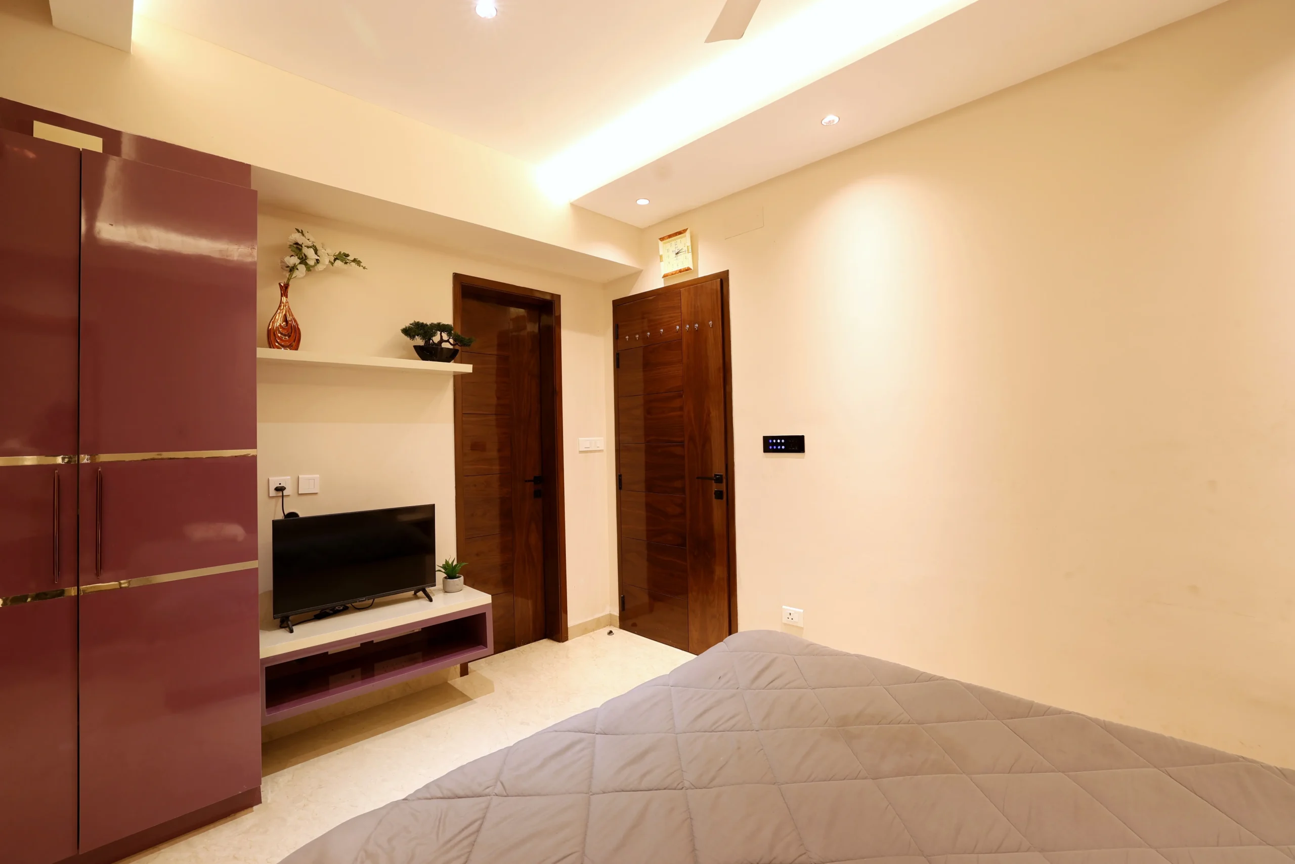 A glossy mauve wardrobe, sleek entertainment unit, and rich wooden doors add sophistication, while recessed and cove lighting create a warm, contemporary ambiance.