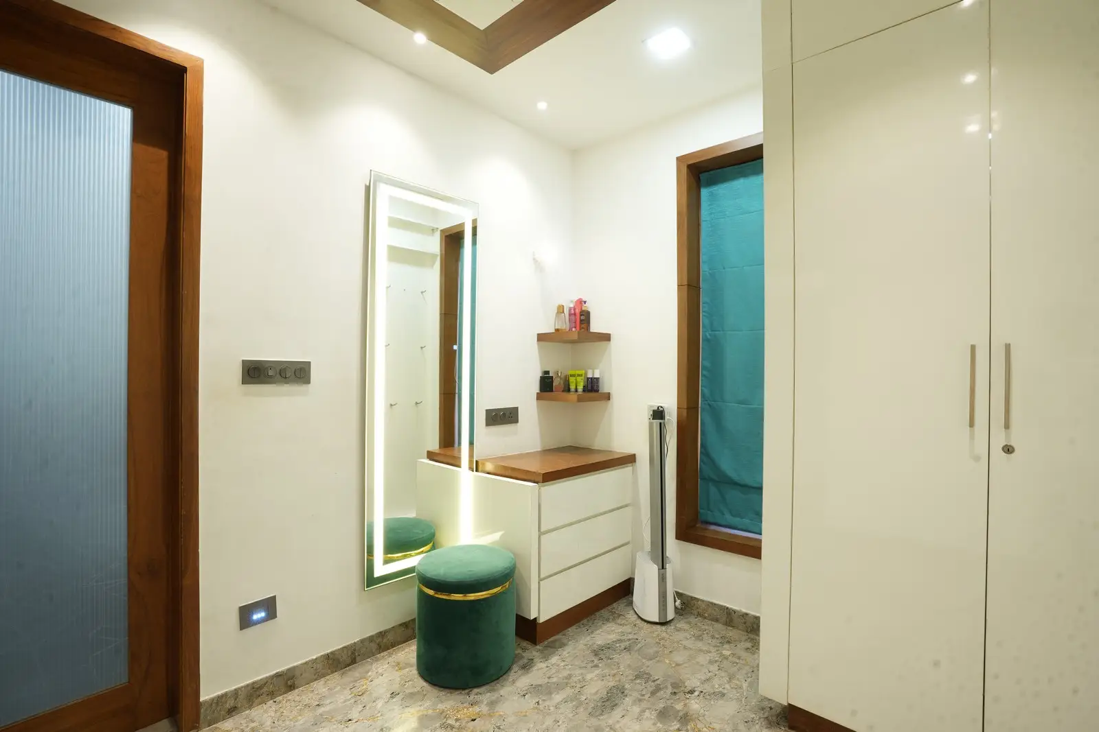 The spacious dressing room features glossy white wardrobes, a convertible dressing mirror, ample storage, and refined veneer detailing for a luxurious, functional experience.
 