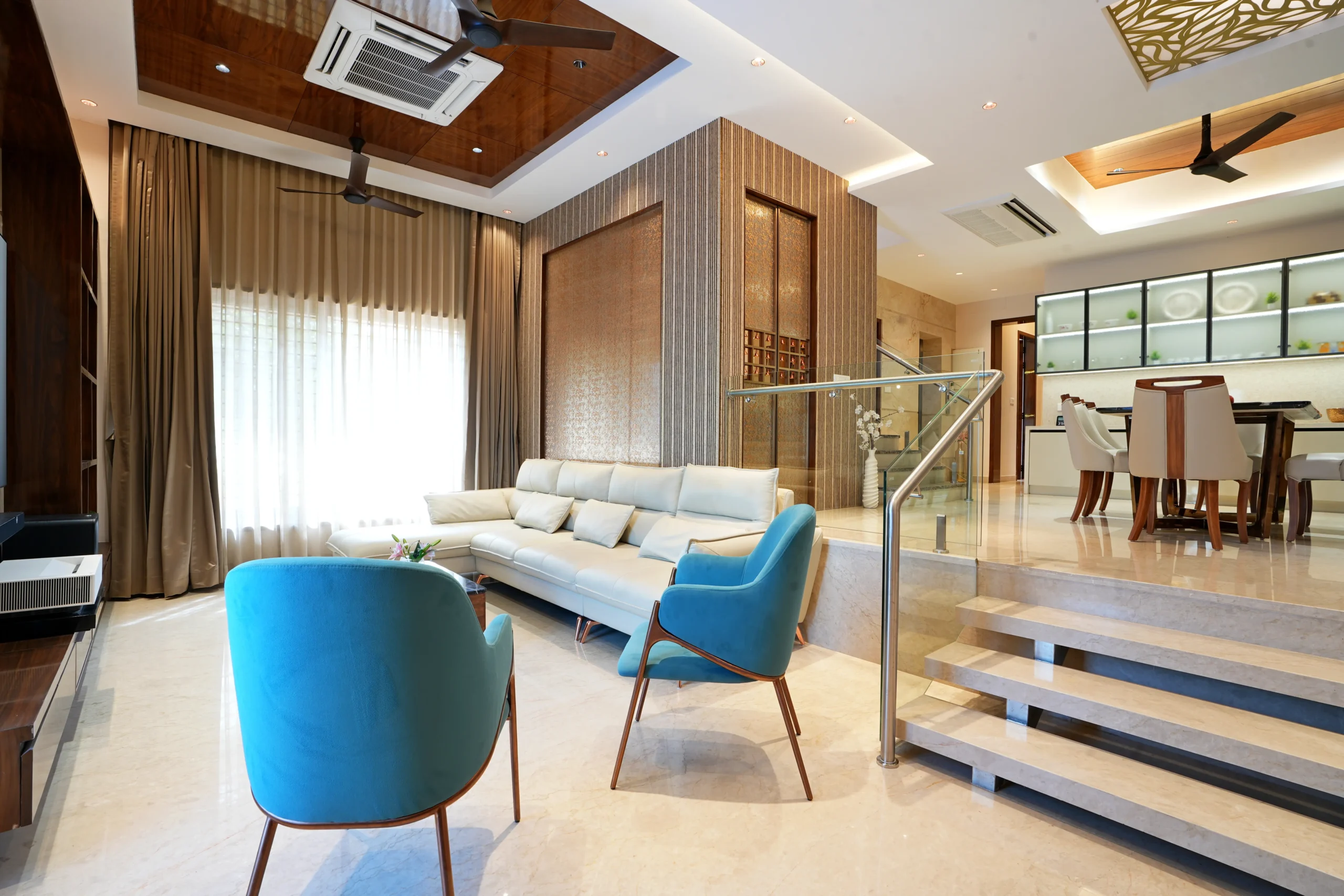 Blue accent chairs add a vibrant contrast to the neutral palette, while marble flooring and glass railings create an open, sophisticated ambiance.