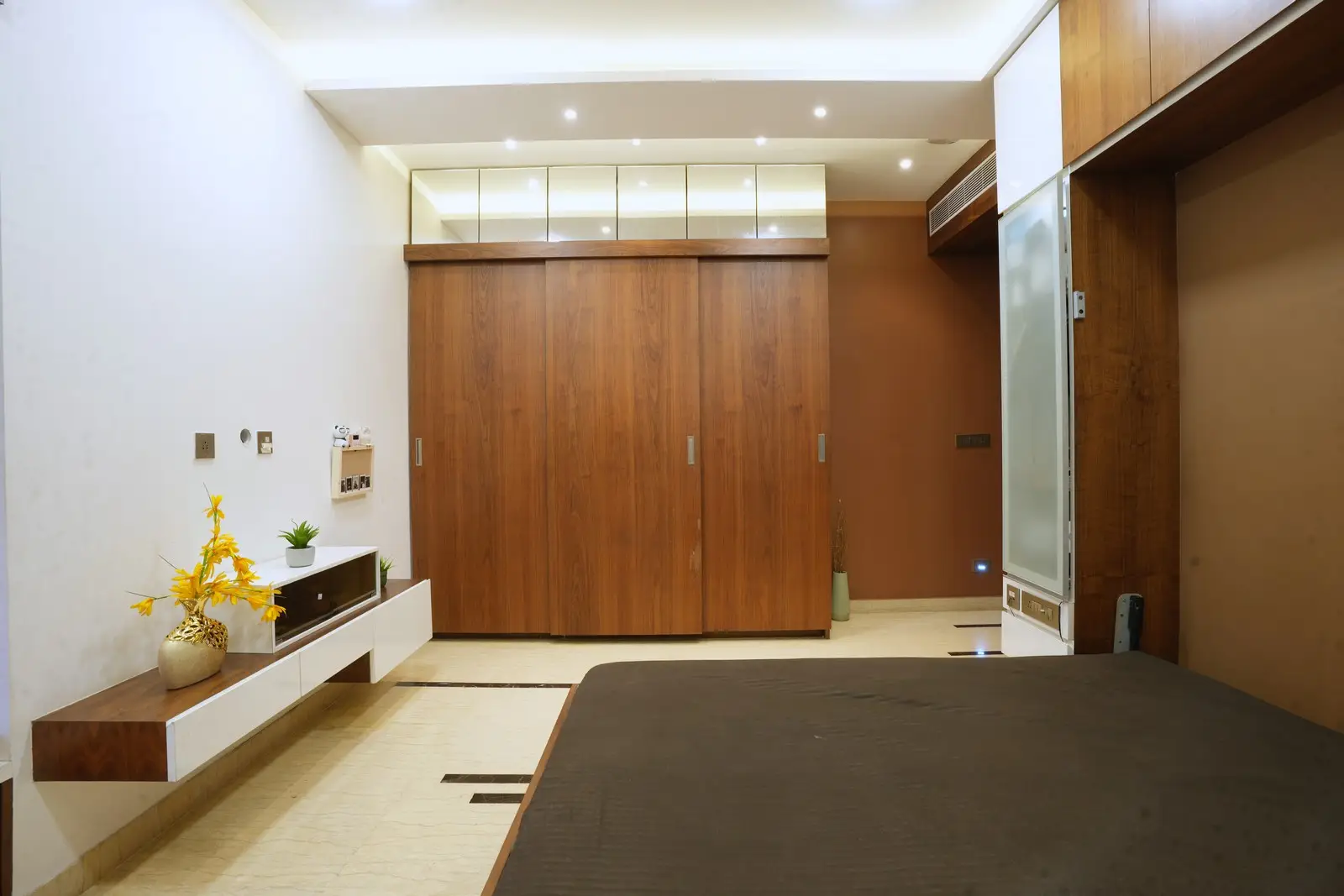 The room features a practical layout, a warm American-walnut wardrobe, and a mirror-finish loft that enhances space and visual appeal.



